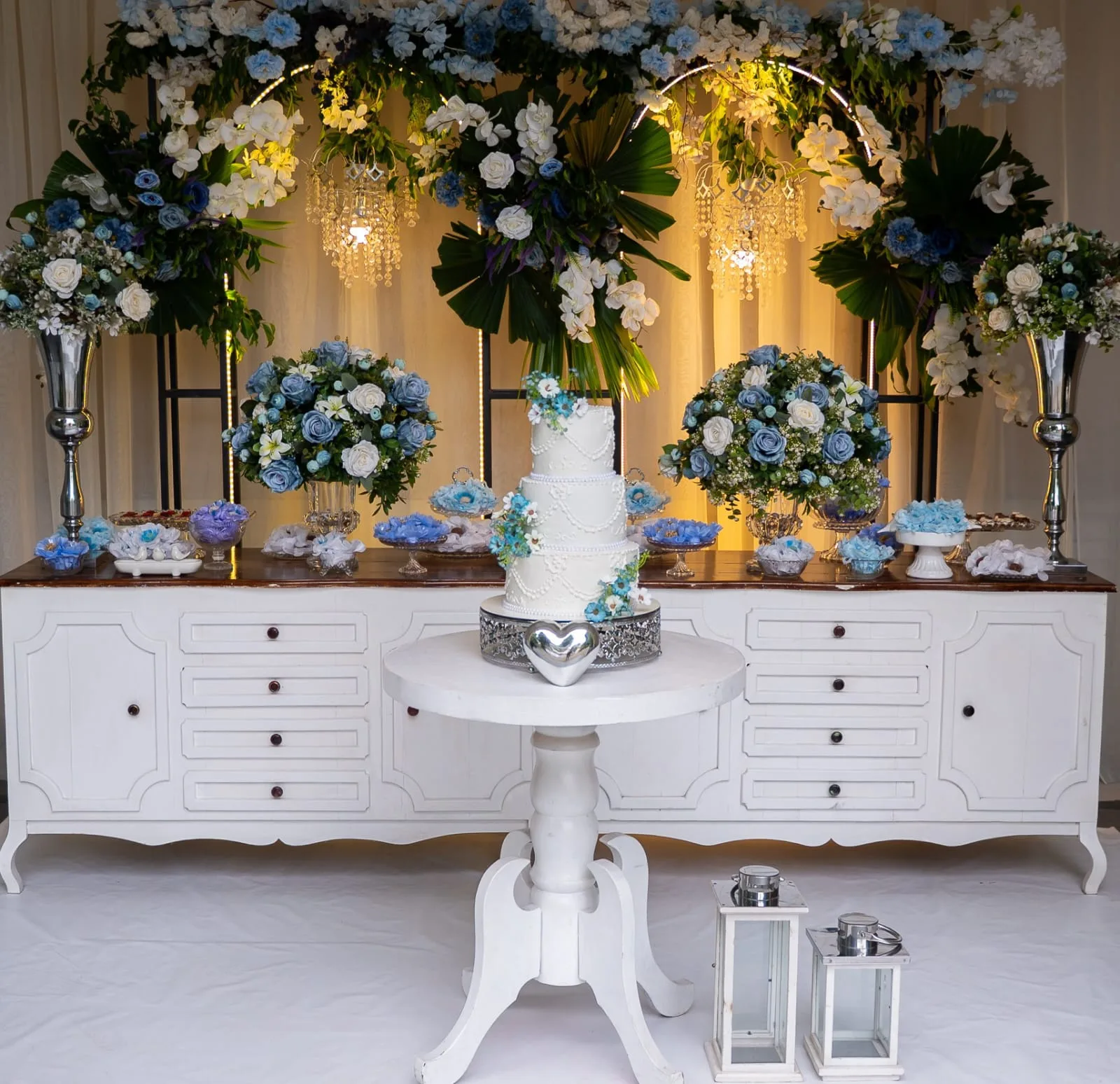 Mesa de bolo com arranjos de flores azuis e brancas